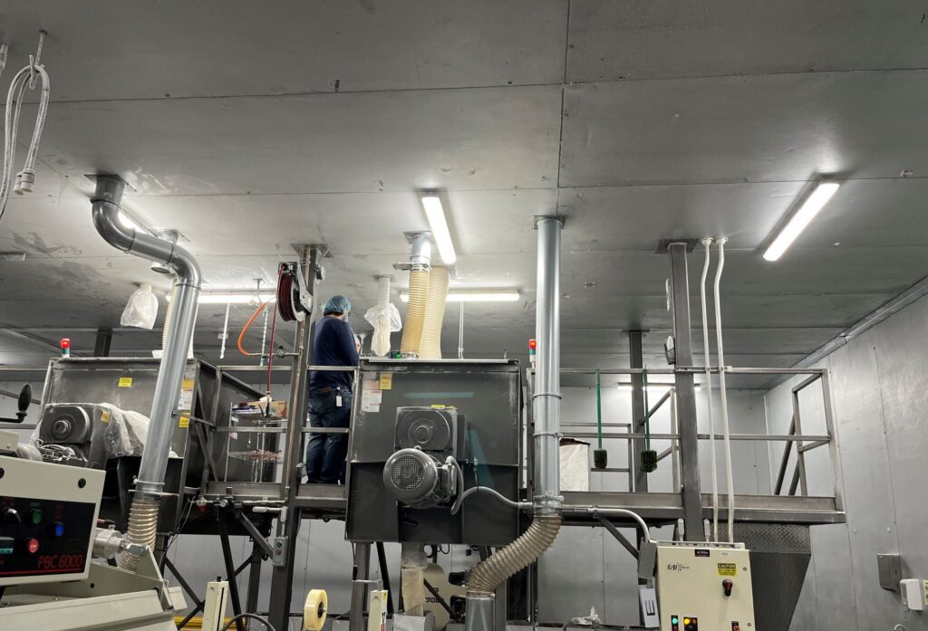 A male employee in a blue shirt stands on top of an industrial machine.