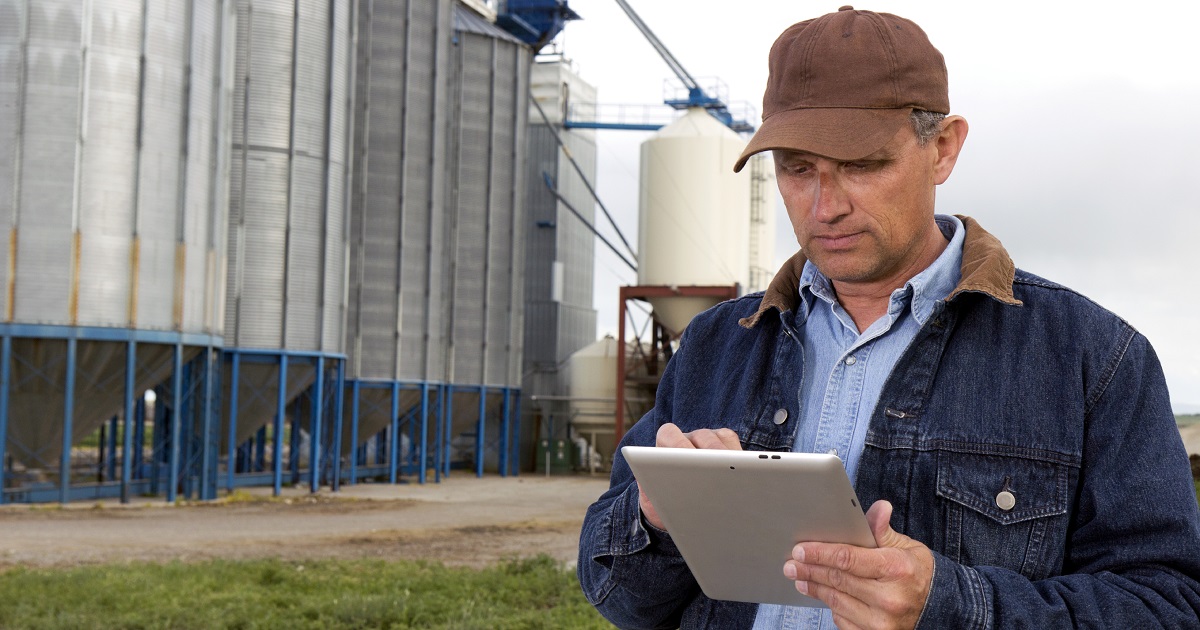 Farmer works on tablet in a field by silos.