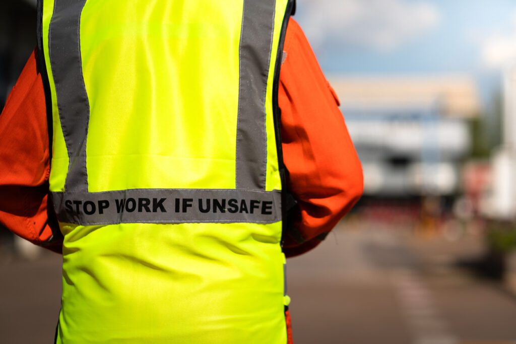 Close-up at "Stop work if unsafe" sign label on back of reflective vest which is wear by a lifting signaler worker.