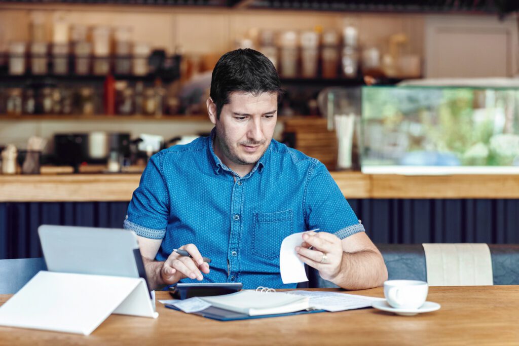 Mature restaurant owner calculating finance and bills of new business – Entrepreneur online using tablet and calculator to work and calculate financial expenses of small coffee shop business start-up