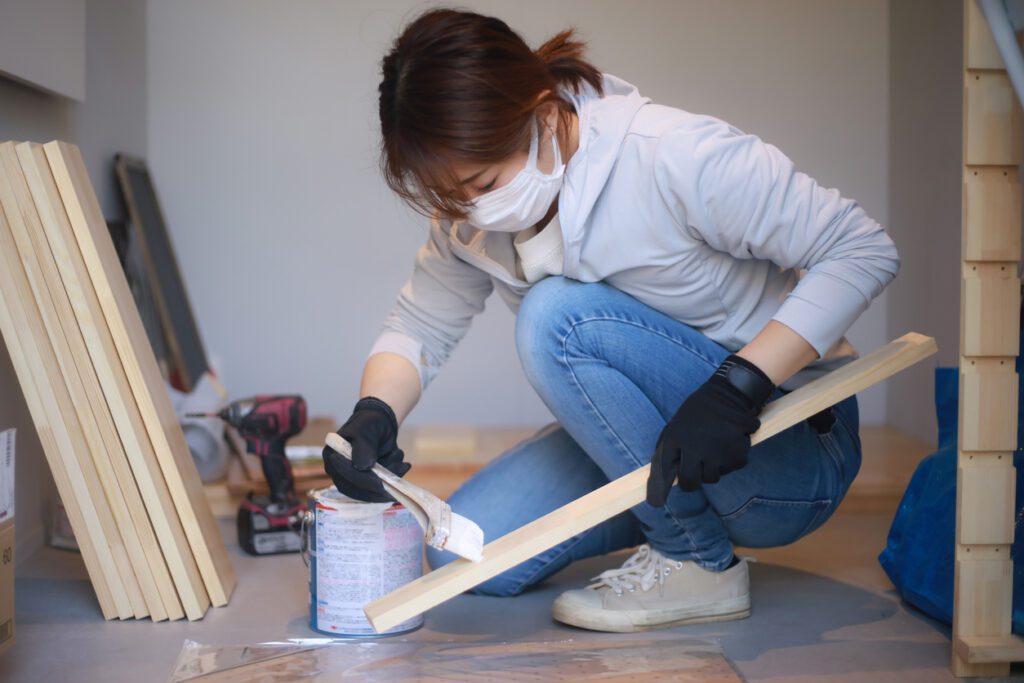 A woman painting lumber with a brush