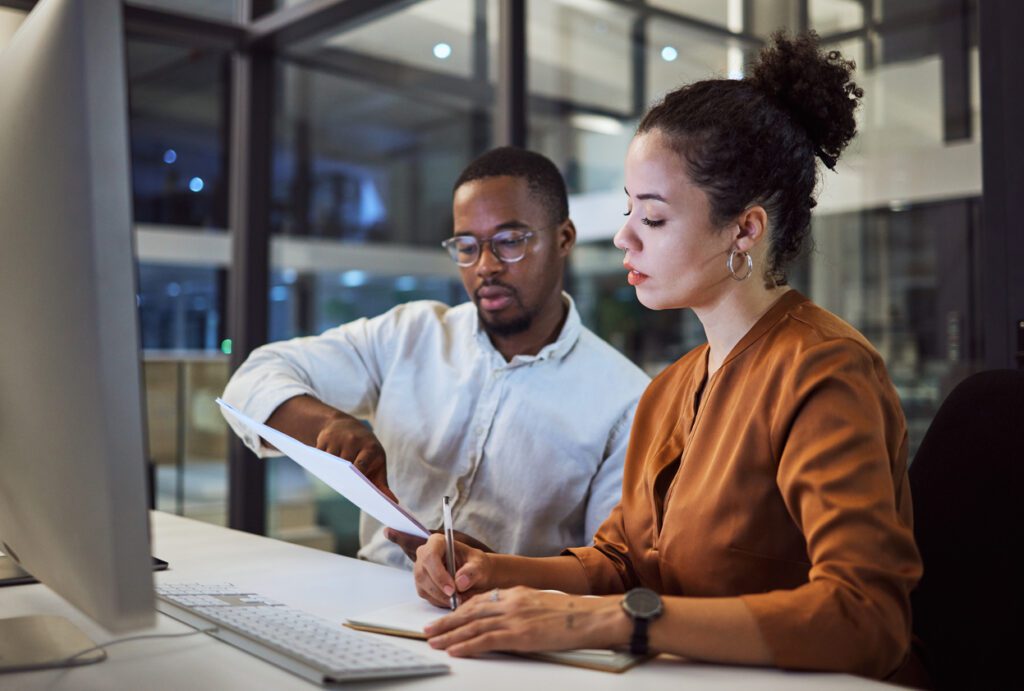 Two employees reading a business document together, black man and latino woman collaborating together in an office
