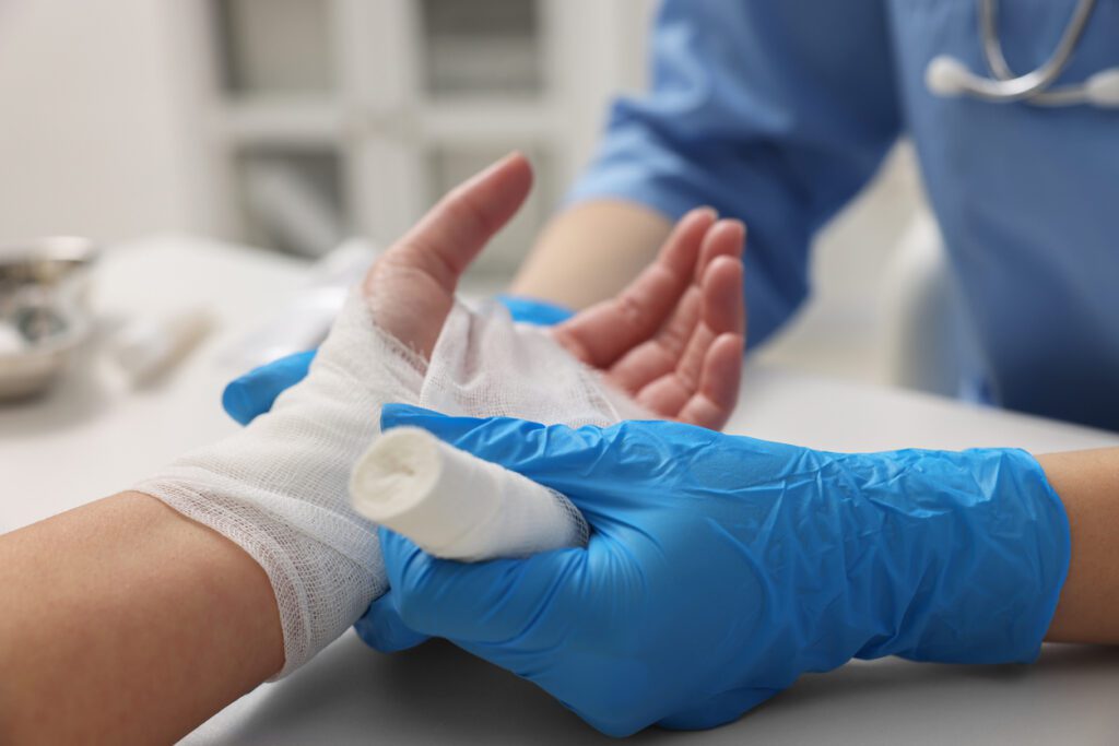 Doctor bandaging patient's hand in hospital, closeup
