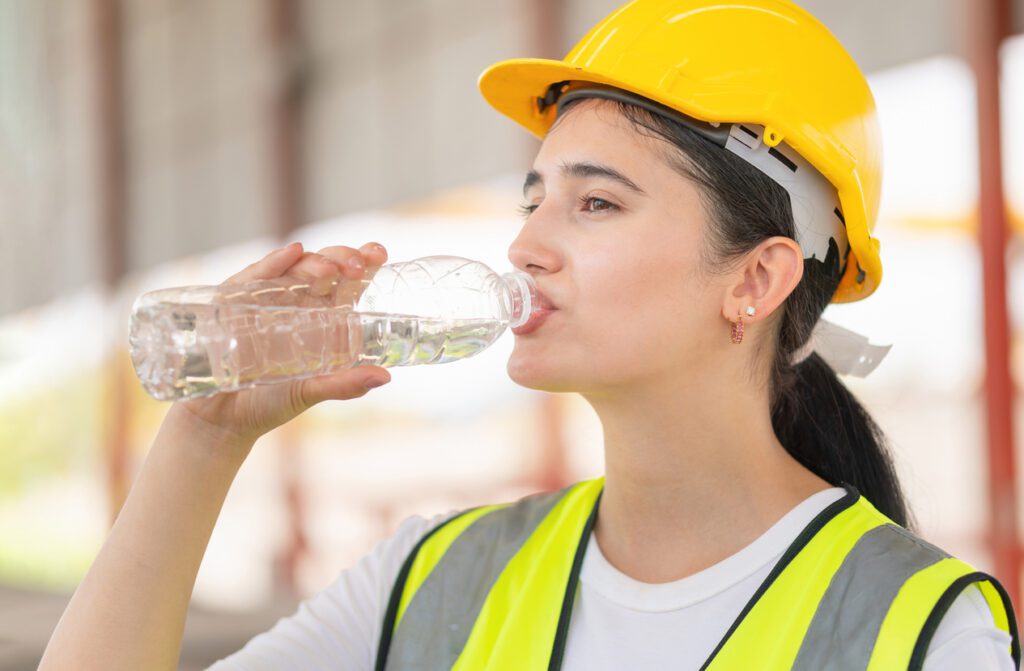 Caucasian female engineer drinking water at the precast factory site, Young forman worker drinking water at construction site stock photo