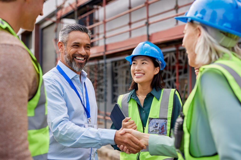 Smiling construction professionals exchanging a handshake as part of their partnership on site. Happy engineer shaking hands at construction site with happy businessman. Handshake between middle eastern construction manager with architect at building site, conclude an agreement.