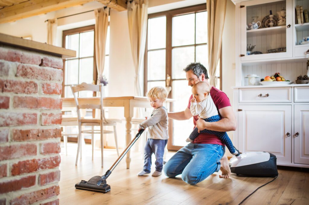 Father and two toddlers cleaning a hardwood floor with a vacuum
