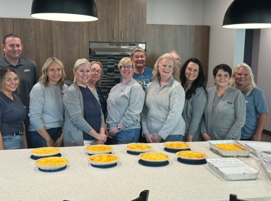 A group of employees poses in front of prepared meals in a kitchen.