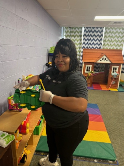 An MEM employee wipes down a green toy in a nursery.